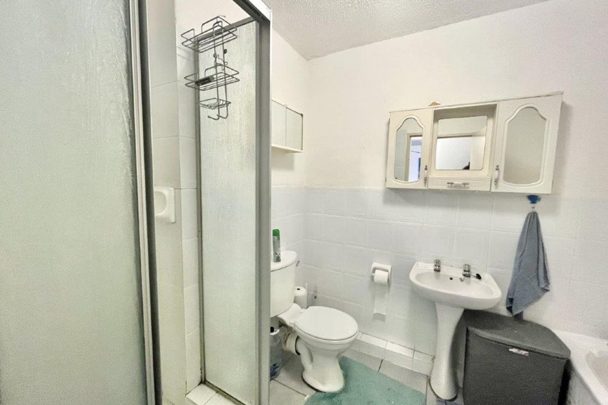 A functional bathroom featuring a shower enclosure, pedestal sink, and toilet, with white wall tiling and dated cabinetry.