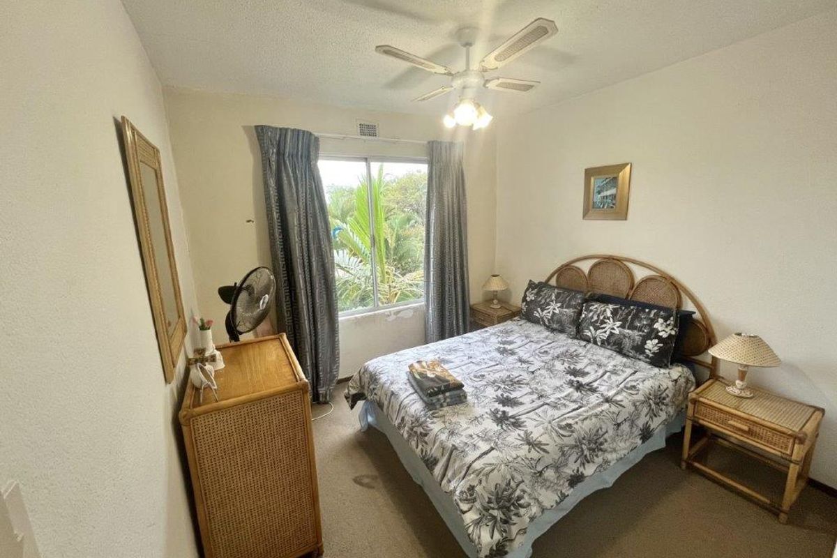 A functional bedroom featuring a ceiling fan, carpeted flooring, and a window providing natural light and garden views.