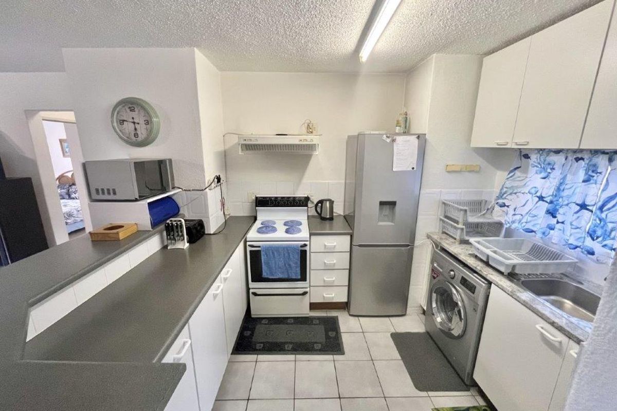 A functional kitchen featuring white cabinetry, tiled flooring, a built-in stove with extractor fan, and integrated space for a washing machine.