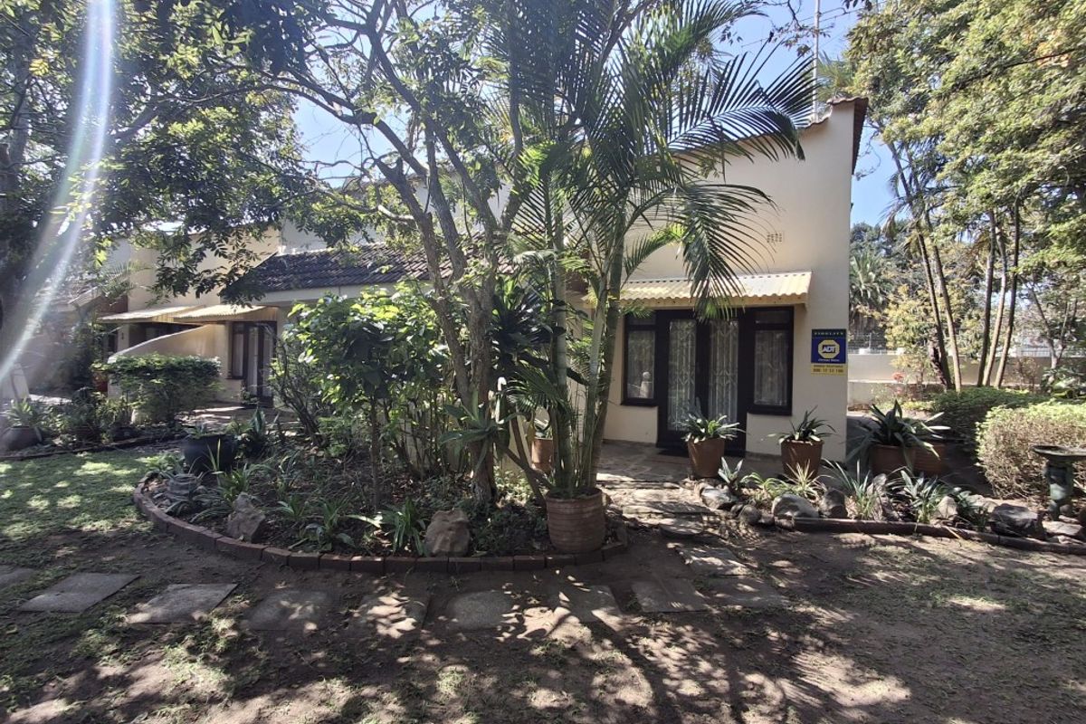 Rear view of the townhouse featuring a garden area, paved pathway, and covered patio entrance with security gate.