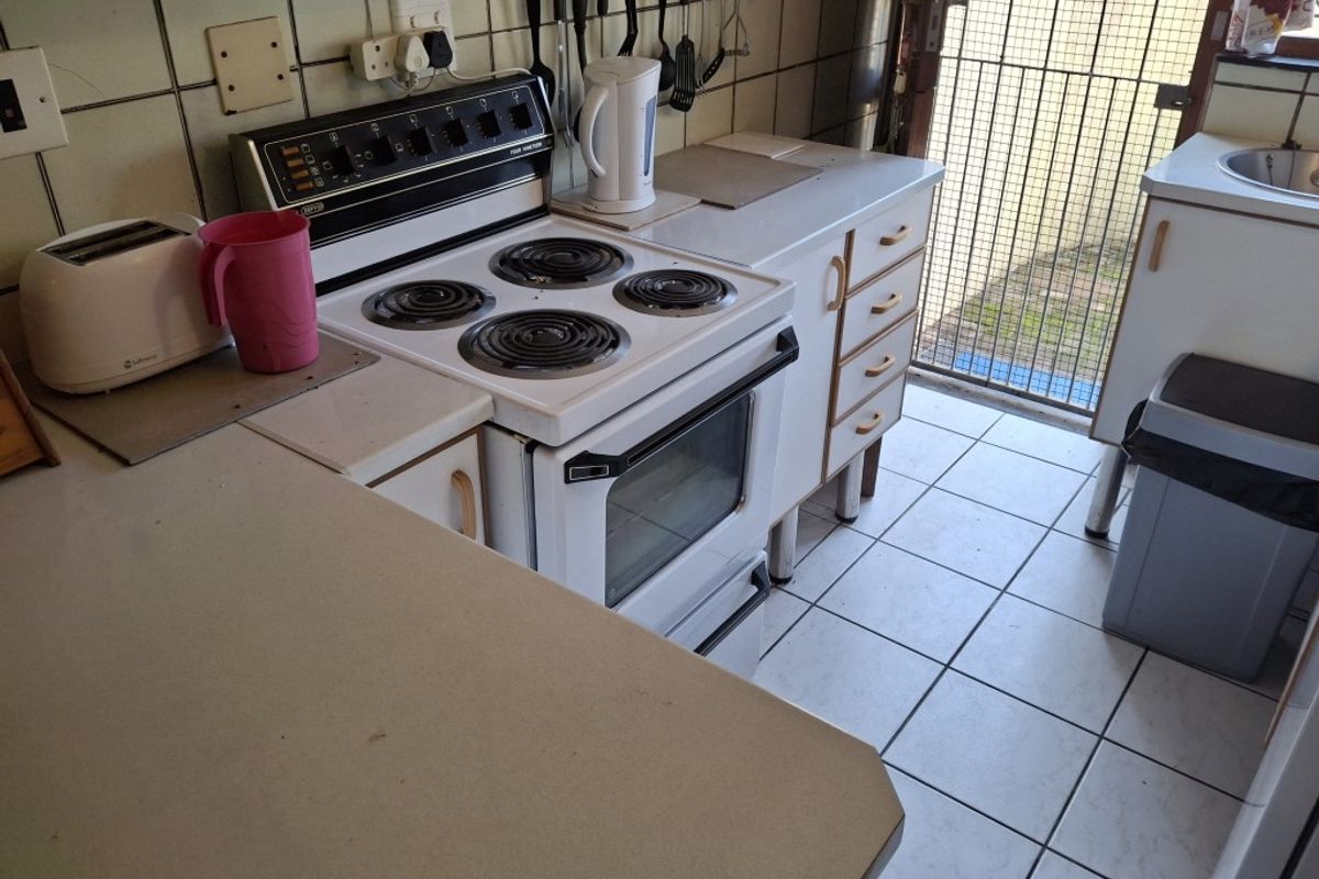 A compact kitchen featuring a freestanding electric stove, tiled backsplash, and built-in cabinetry with direct access to an outdoor area via a security gate.