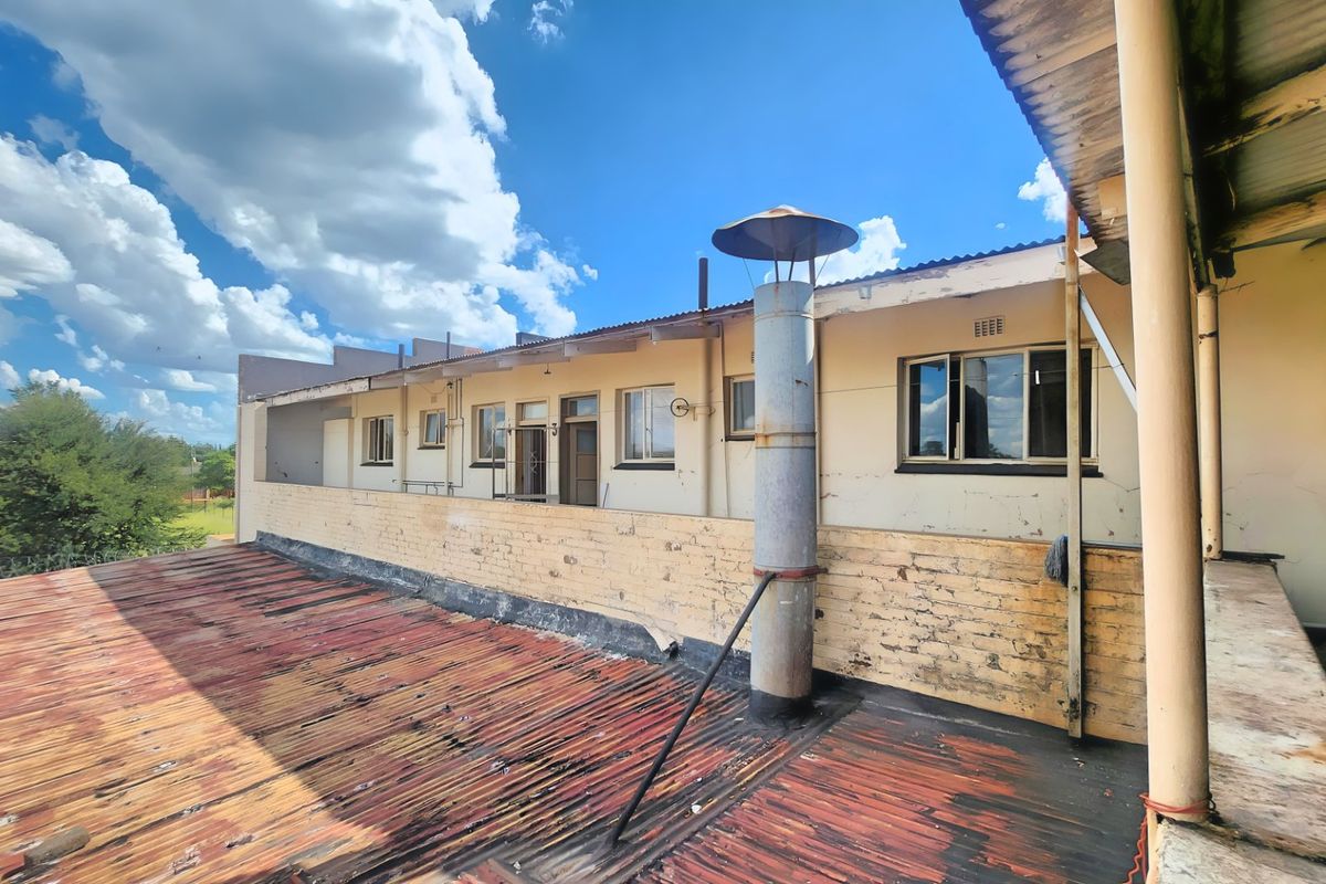 Rear exterior view of a commercial building featuring a weathered corrugated metal roof, brick parapet wall, and exposed metal chimney flue.