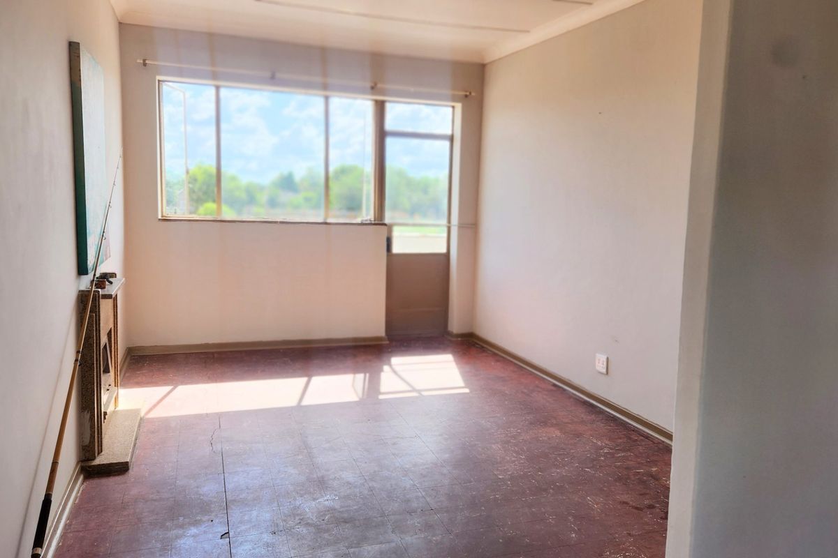 An empty living room featuring a fireplace, large windows, and direct access to the exterior, offering a blank canvas for renovation.