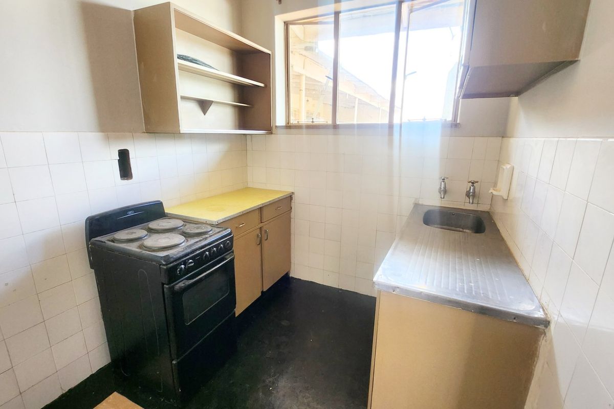 A compact, dated kitchen featuring a stainless steel sink, tiled splashback, built-in cabinetry, and an electric stove.