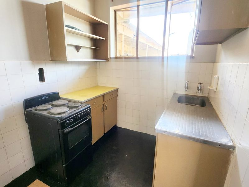 A compact, dated kitchen featuring a stainless steel sink, tiled splashback, built-in cabinetry, and an electric stove.