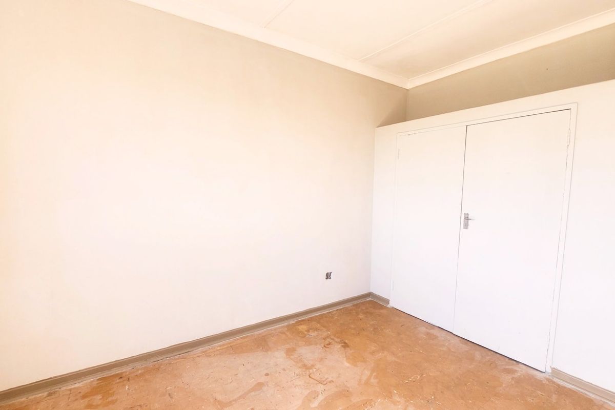 An empty bedroom featuring a built-in wardrobe, coved ceilings, and worn flooring, offering a blank canvas for renovation and interior design.
