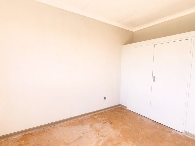 An empty bedroom featuring a built-in wardrobe, coved ceilings, and worn flooring, offering a blank canvas for renovation and interior design.