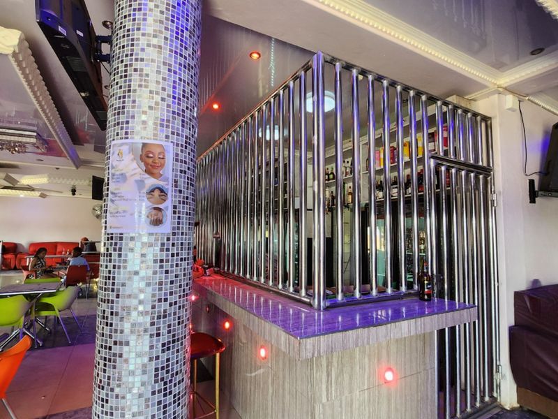 A commercial bar area featuring a mosaic-tiled support pillar, a stainless steel security cage enclosure, and integrated recessed ceiling lighting.