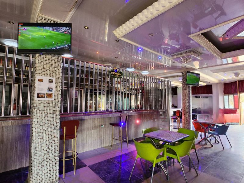 Commercial bar area featuring a built-in counter, mosaic-tiled support columns, and a decorative suspended ceiling with integrated lighting.