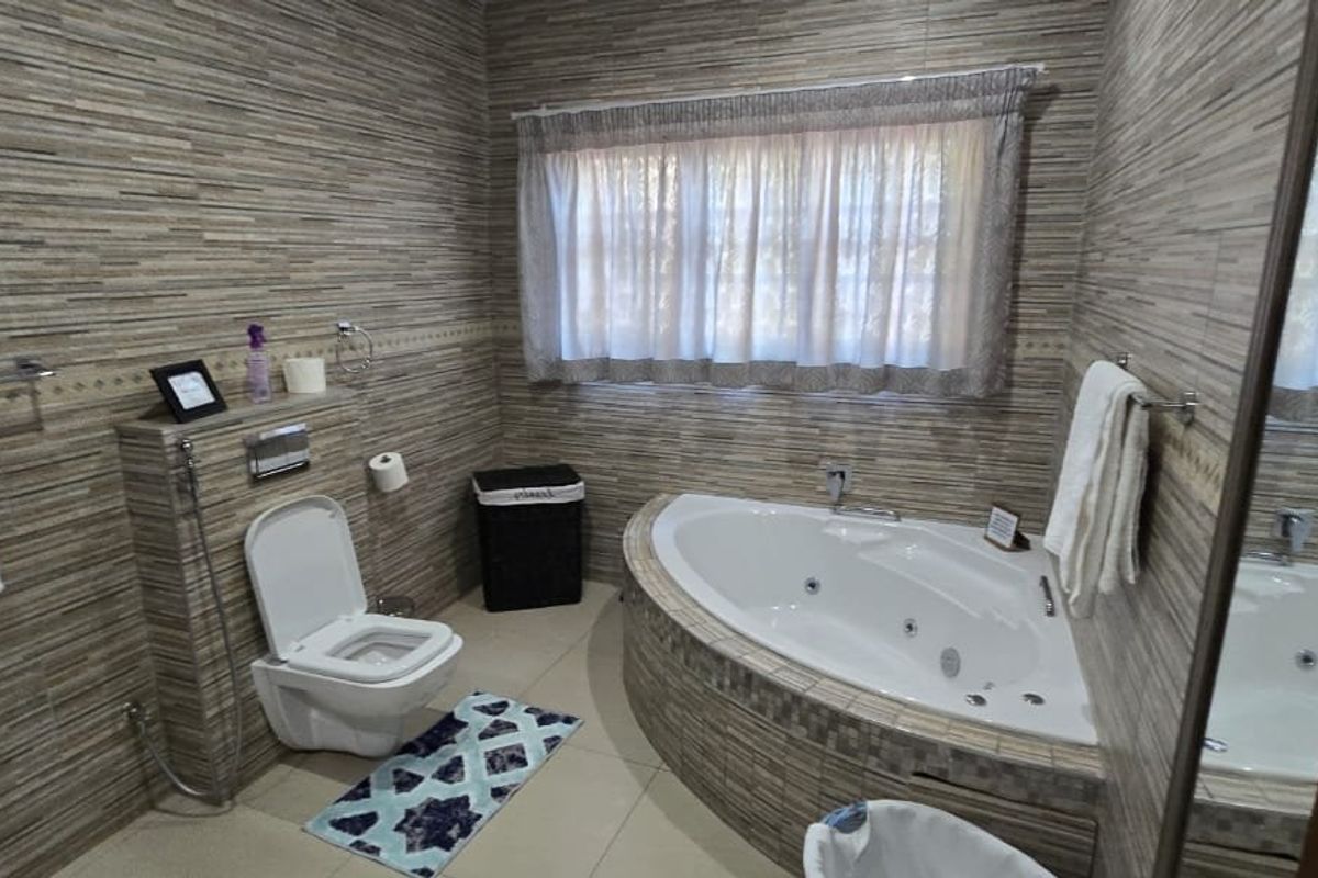 A well-maintained bathroom featuring a corner spa bath, wall-mounted toilet, and floor-to-ceiling tiled finishes.