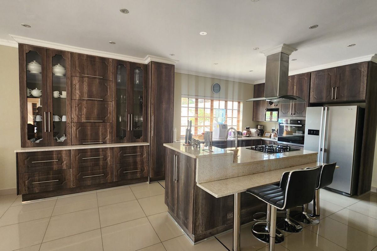 Spacious kitchen featuring dark wood cabinetry, stone countertops, a central island with breakfast bar, and integrated stainless steel appliances.