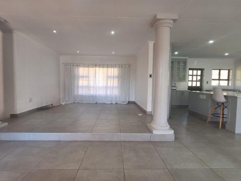 Spacious open-plan living and kitchen area featuring tiled flooring, decorative columns, and a functional kitchen island with built-in cabinetry.