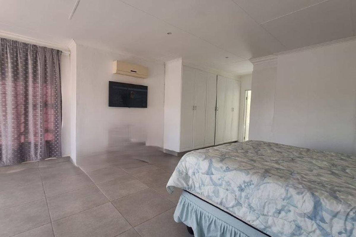 Spacious bedroom featuring neutral tiled flooring, built-in cupboards for storage, and an integrated air conditioning unit.
