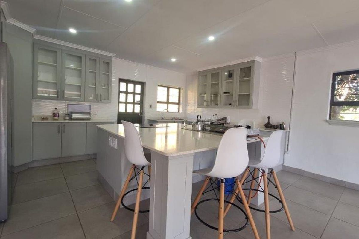 A modern, well-lit kitchen featuring a central island with stone countertops, ample built-in cabinetry, and tiled flooring.