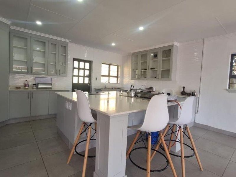 A modern, well-lit kitchen featuring a central island with stone countertops, ample built-in cabinetry, and tiled flooring.