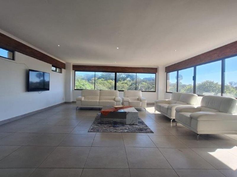 Spacious living room featuring large format floor tiles, recessed downlighting, and expansive windows with timber pelmets offering natural light and garden views.