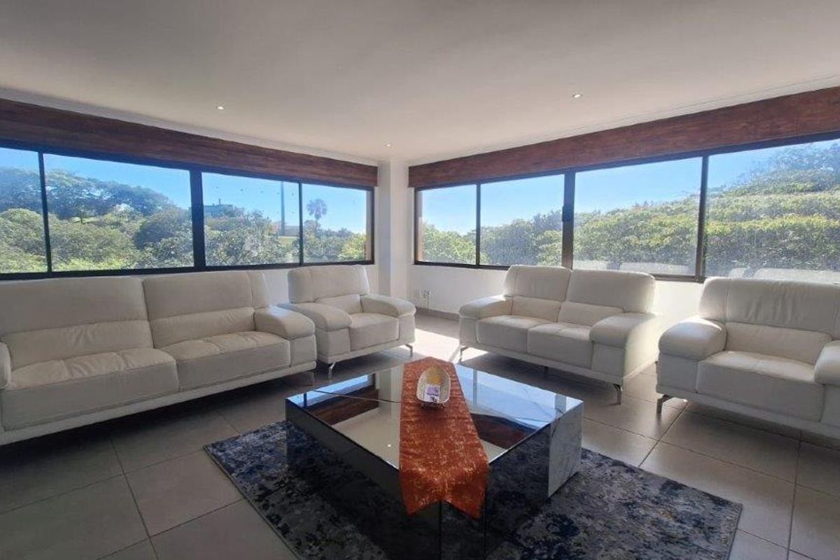 Spacious living room featuring large windows with timber pelmets, recessed downlights, and neutral tiled flooring, offering abundant natural light and scenic views.