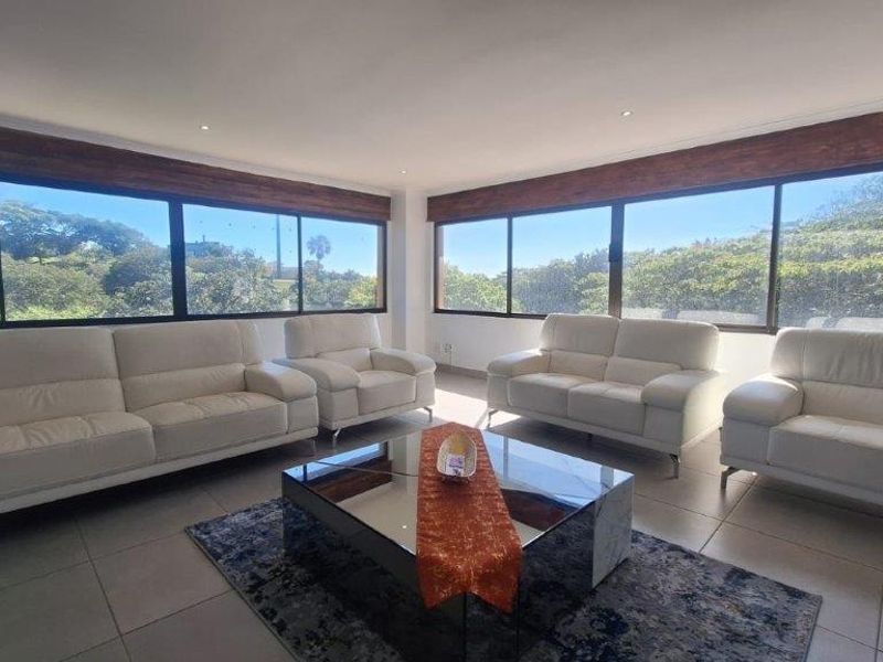 Spacious living room featuring large windows with timber pelmets, recessed downlights, and neutral tiled flooring, offering abundant natural light and scenic views.