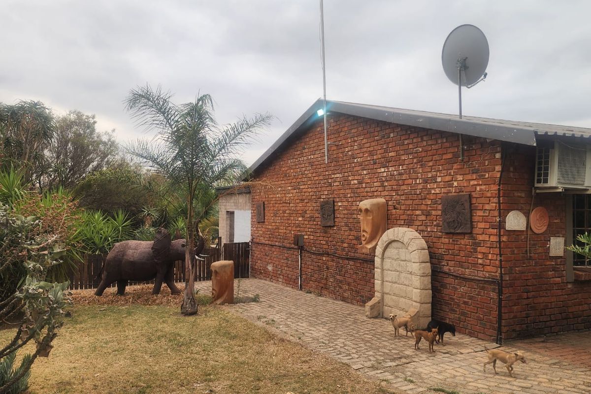 Rear exterior view of a face brick farm building featuring a paved walkway, satellite dish, and established garden area.