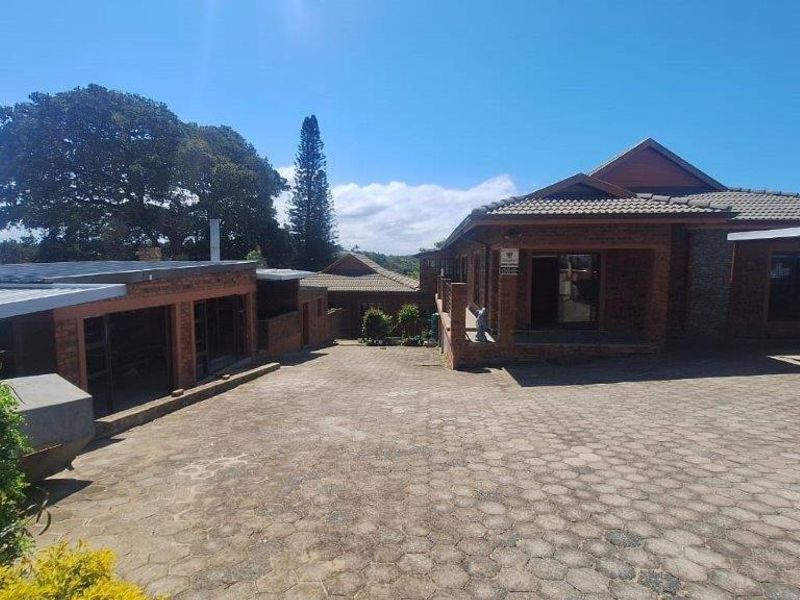 Exterior view of the property featuring a large paved driveway, brick facade, and multiple structures under a tiled roof.