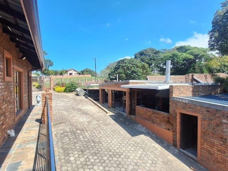 An exterior view of the property featuring exposed brick walls, a paved driveway, and a covered patio area.