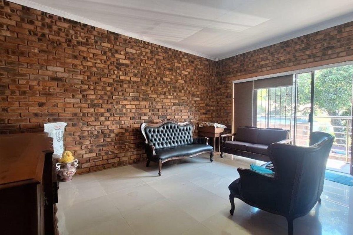 Spacious living room featuring a prominent exposed face-brick feature wall, large sliding glass doors, and neutral floor tiling.