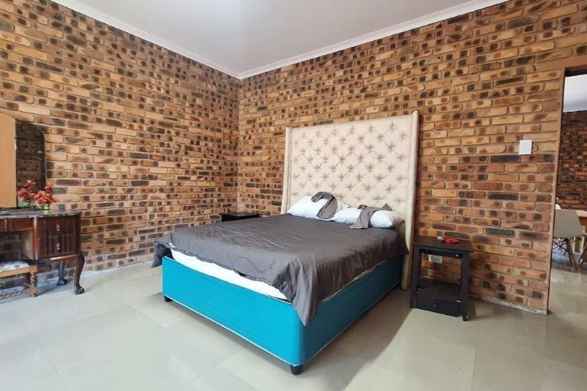 Spacious bedroom featuring exposed face-brick walls and tiled flooring, offering a rustic aesthetic with direct access to an adjacent dining area.