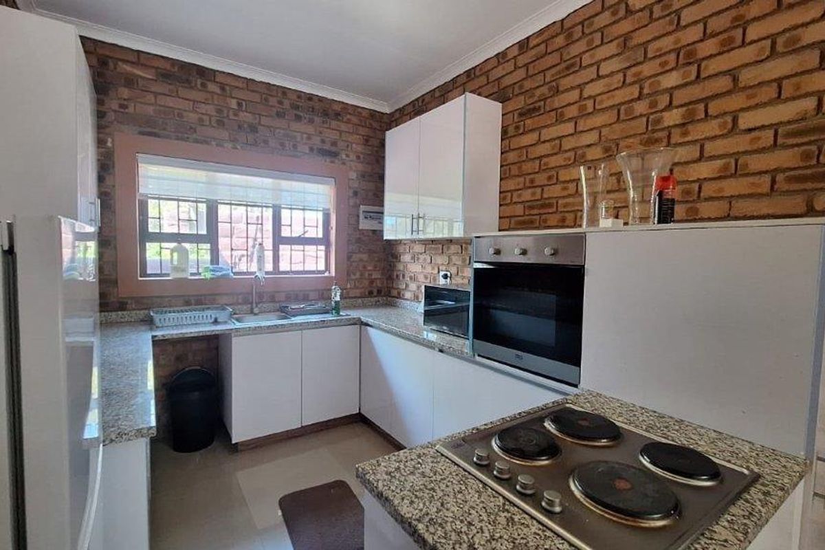 A functional kitchen featuring exposed brick walls, granite countertops, white cabinetry, a built-in oven, and a four-plate electric hob.