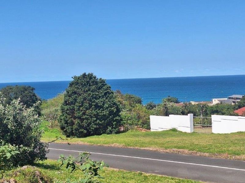 A scenic view overlooking the coastal landscape, featuring a paved road, lush greenery, and a clear view of the ocean horizon.