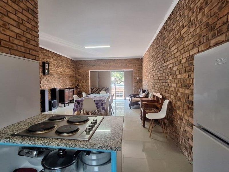 Open-plan living and dining area featuring exposed brick walls, tiled flooring, and a functional kitchen with a built-in hob and granite countertop.