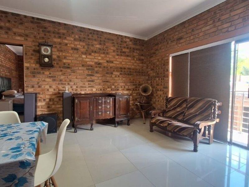 Open plan living and dining area featuring exposed brick walls, large format floor tiles, and sliding glass doors leading to an outdoor space.