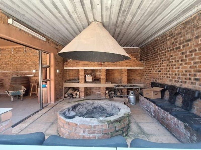Covered outdoor entertainment area featuring a central brick fire pit, built-in brick seating, and a large suspended metal extractor hood.
