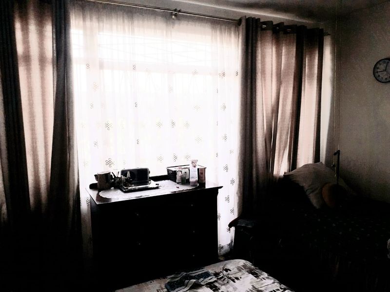 A bedroom interior featuring large windows with layered curtains, providing natural light to the space.