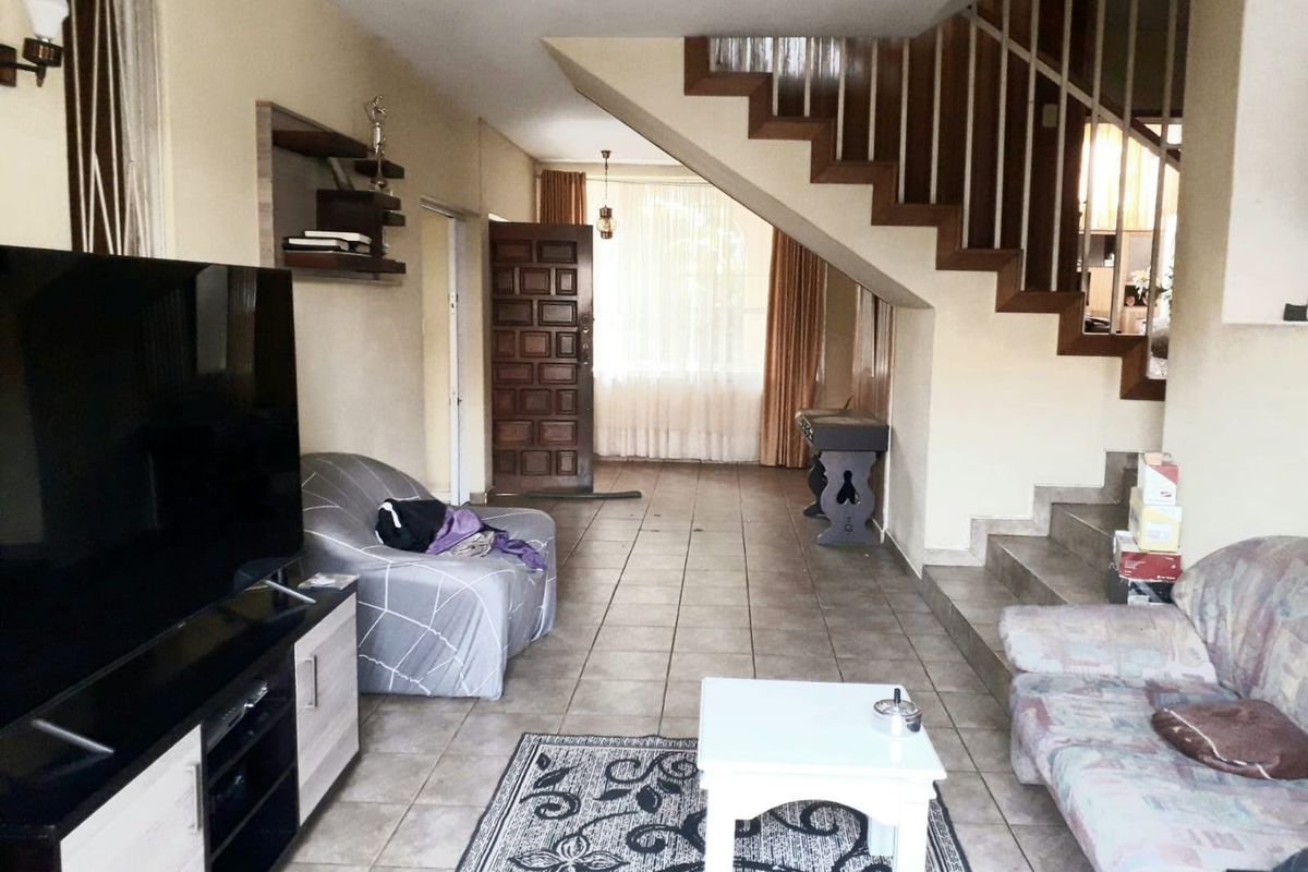 Spacious living area featuring tiled flooring, a prominent wooden staircase with balustrade, and direct access to the main entrance.