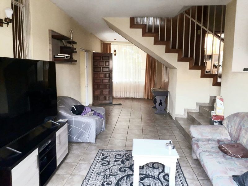 Spacious living area featuring tiled flooring, a prominent wooden staircase with balustrade, and direct access to the main entrance.