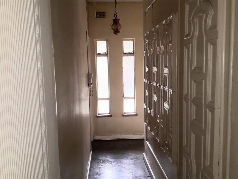A narrow hallway featuring decorative wall paneling, a pendant light fixture, and dual casement windows, showing signs of wear on the flooring and walls.