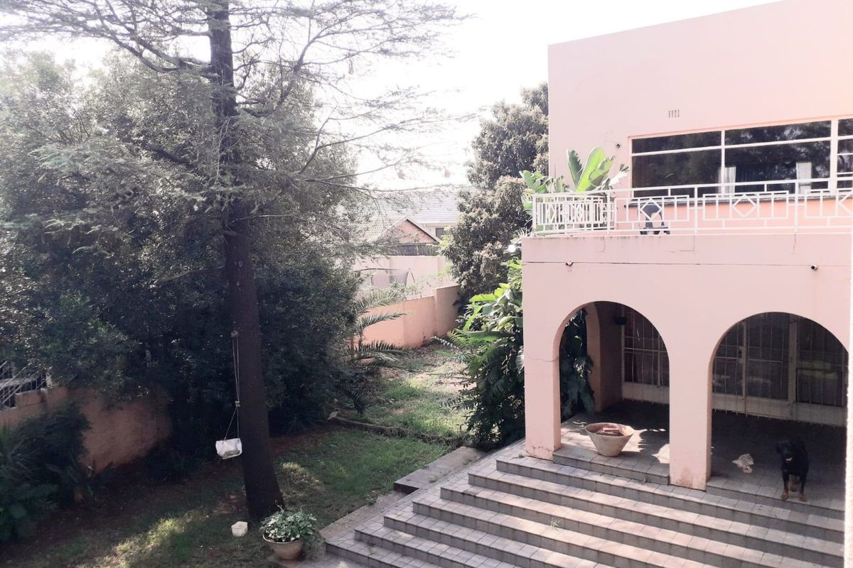 Rear view of a commercial property featuring a covered arched patio, tiled stairs leading to the garden, and an upper-level balcony with metal railings.