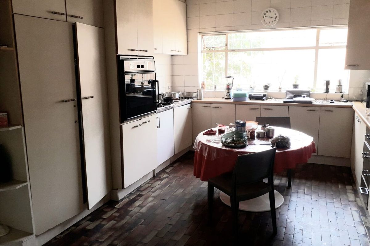 A dated kitchen featuring built-in cabinetry, a wall-mounted oven, tiled backsplash, and traditional brick flooring, offering significant potential for modernization.