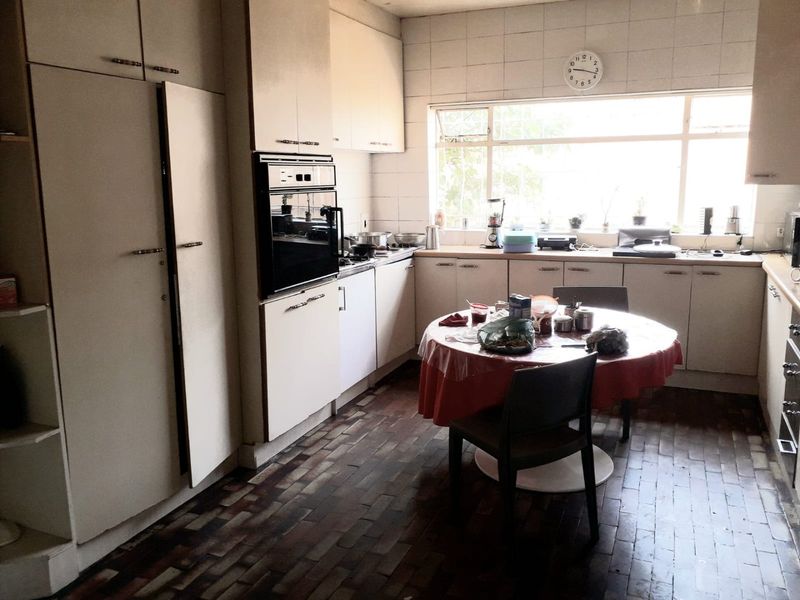 A dated kitchen featuring built-in cabinetry, a wall-mounted oven, tiled backsplash, and traditional brick flooring, offering significant potential for modernization.