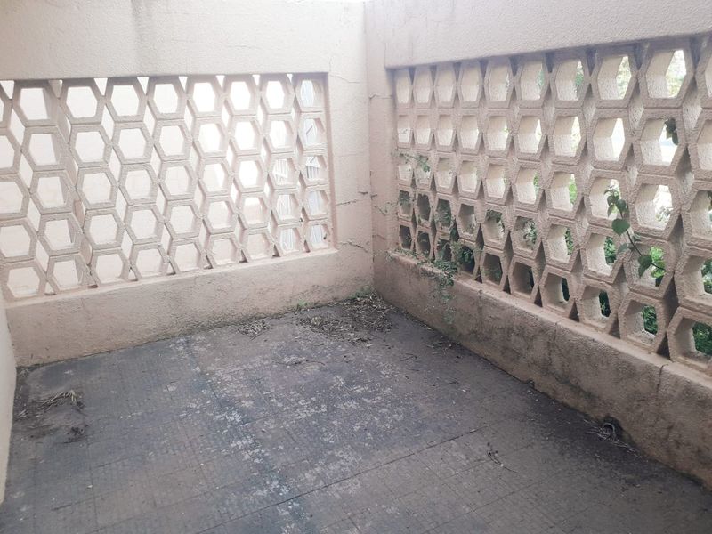 A small outdoor patio area featuring decorative breeze block walls and tiled flooring, currently in need of maintenance and cleaning.