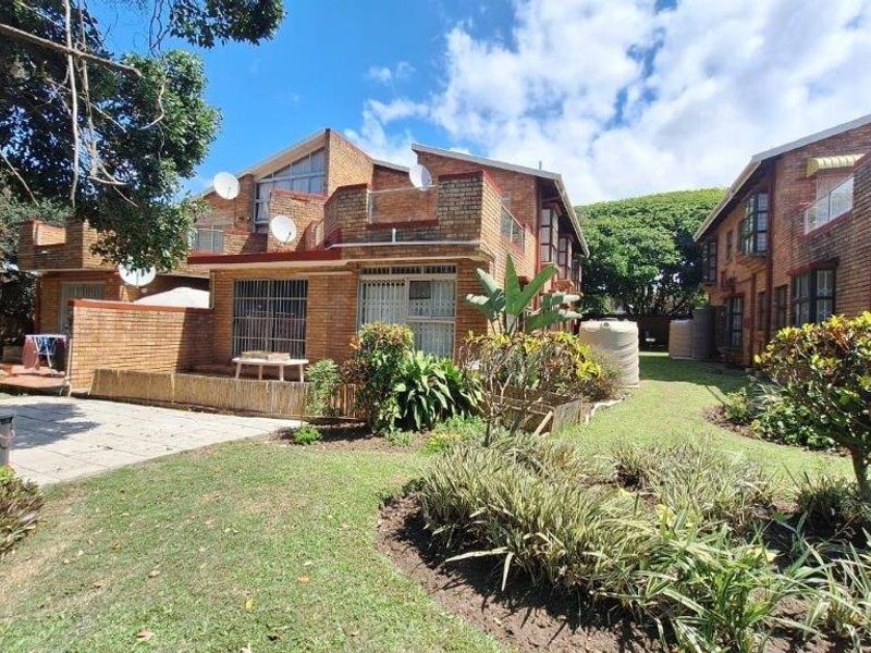 Rear view of a face brick townhouse complex featuring a paved patio area, landscaped garden, and exterior water storage tanks.