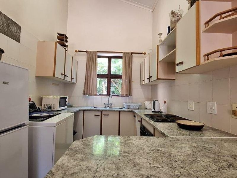 A functional kitchen featuring laminate countertops, built-in cabinetry, a stainless steel sink, and an electric hob with tiled splashbacks.