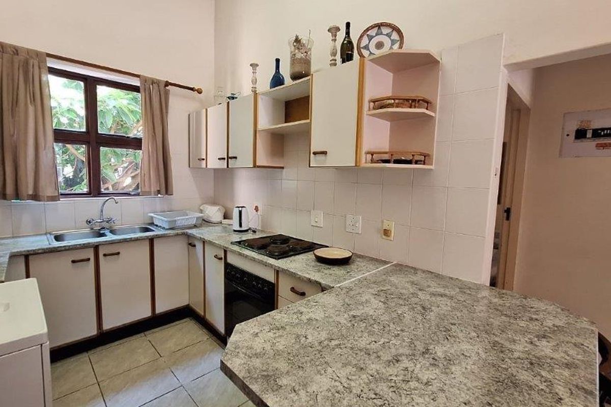A functional kitchen featuring built-in cabinetry, laminate countertops, a double basin sink, and an integrated oven with hob, finished with tiled splashbacks.