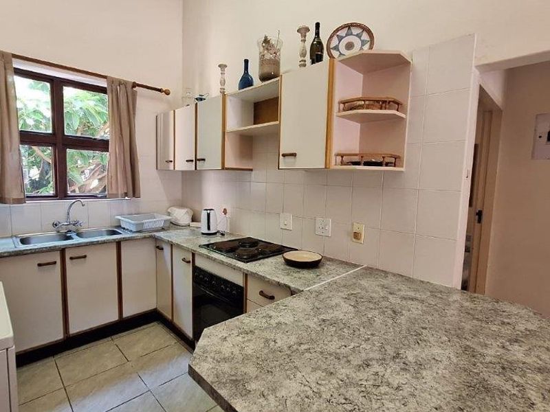 A functional kitchen featuring built-in cabinetry, laminate countertops, a double basin sink, and an integrated oven with hob, finished with tiled splashbacks.