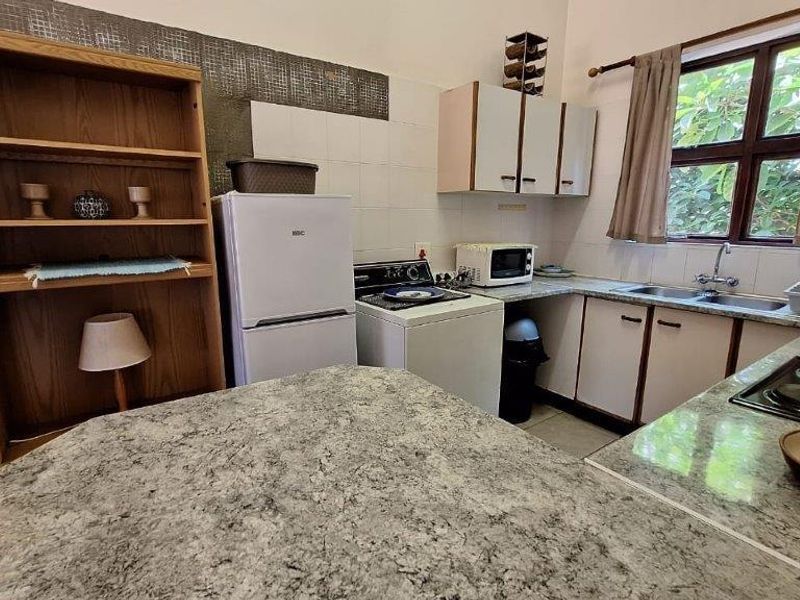 A dated kitchen featuring laminate countertops, a double basin sink, and built-in cabinetry with tiled splashbacks, offering potential for a modern renovation.