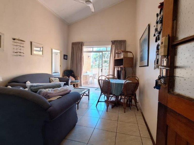 A living room featuring tiled flooring, a vaulted ceiling, and a sliding glass door providing access to an outdoor patio area.