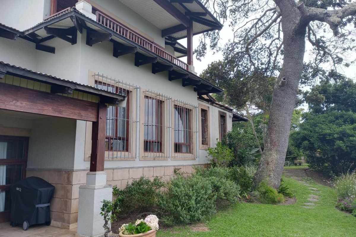 Side elevation of the house featuring a covered patio area, timber roof detailing, and security bars on the windows, set within a landscaped garden.