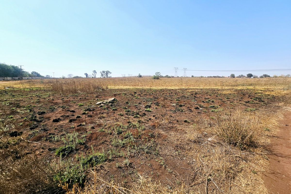 A wide-angle view of a vacant residential plot featuring dry, undeveloped land under a clear blue sky.