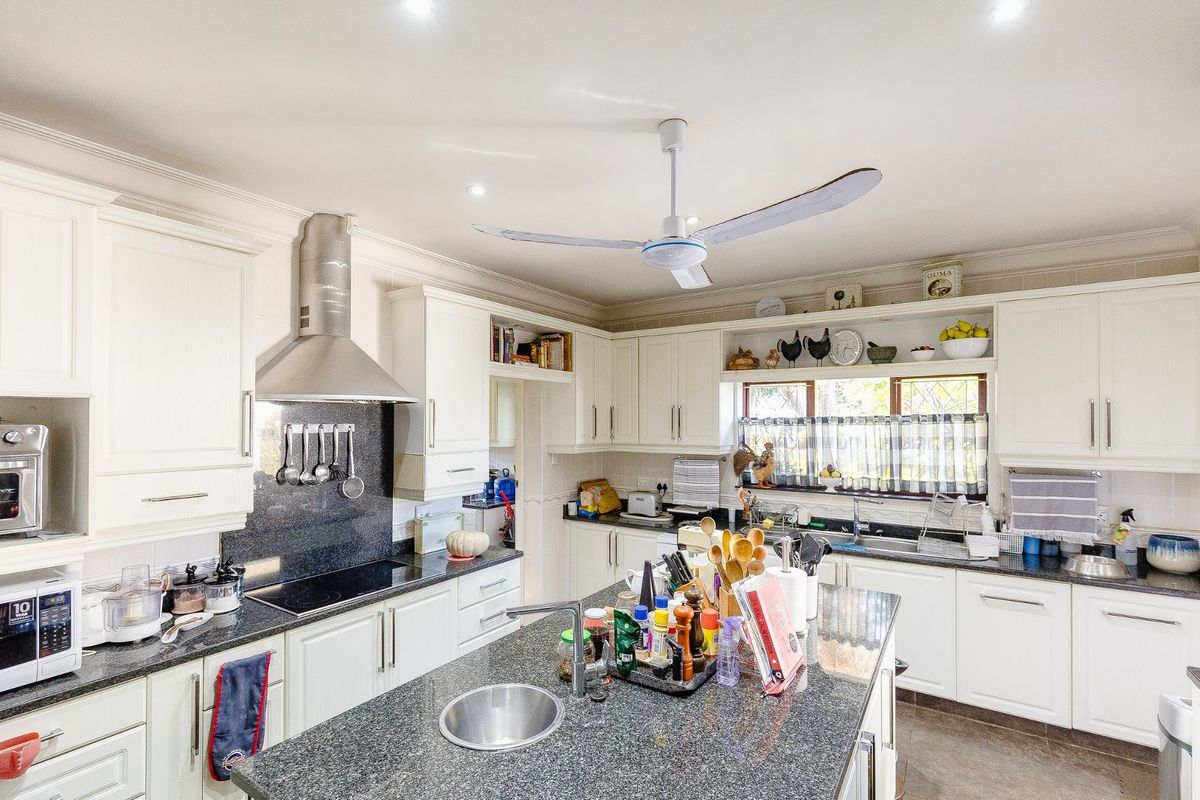 A well-appointed kitchen featuring granite countertops, ample white cabinetry, a central island with a prep sink, and integrated stainless steel appliances.