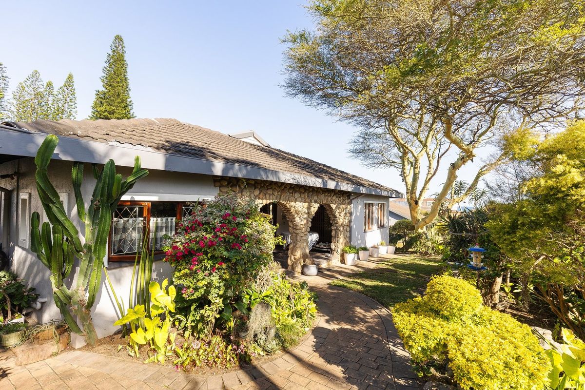 A charming rear exterior view featuring a stone-clad arched patio, tiled roof, and a well-maintained garden with a paved walkway.